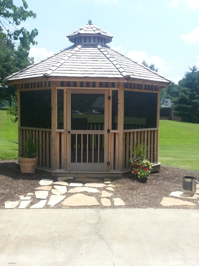 A wooden gazebo with a screened in porch sits in the middle of a grassy field