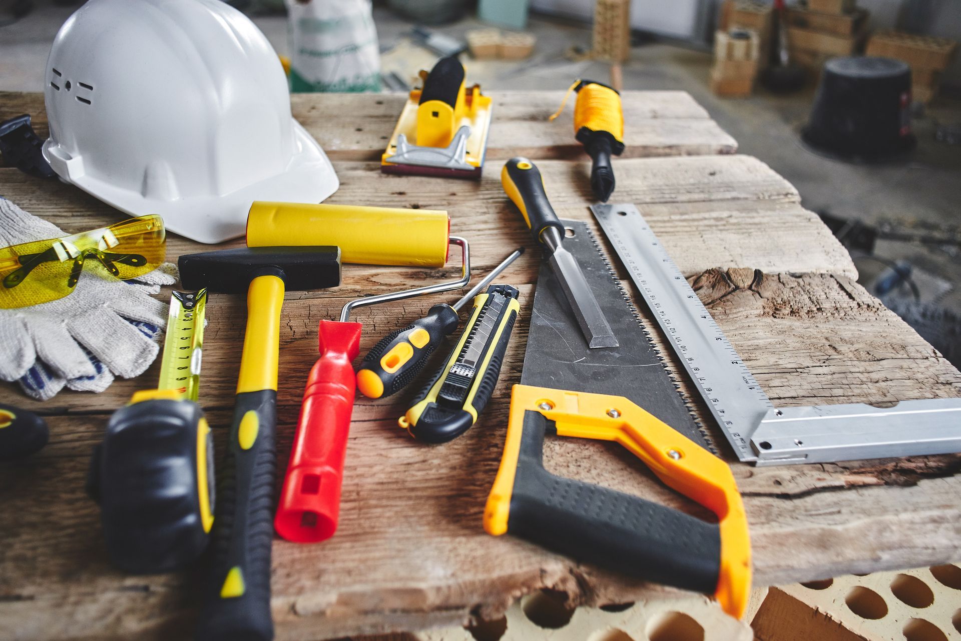 Assorted construction tools and safety gear on wooden workbench for home renovation.