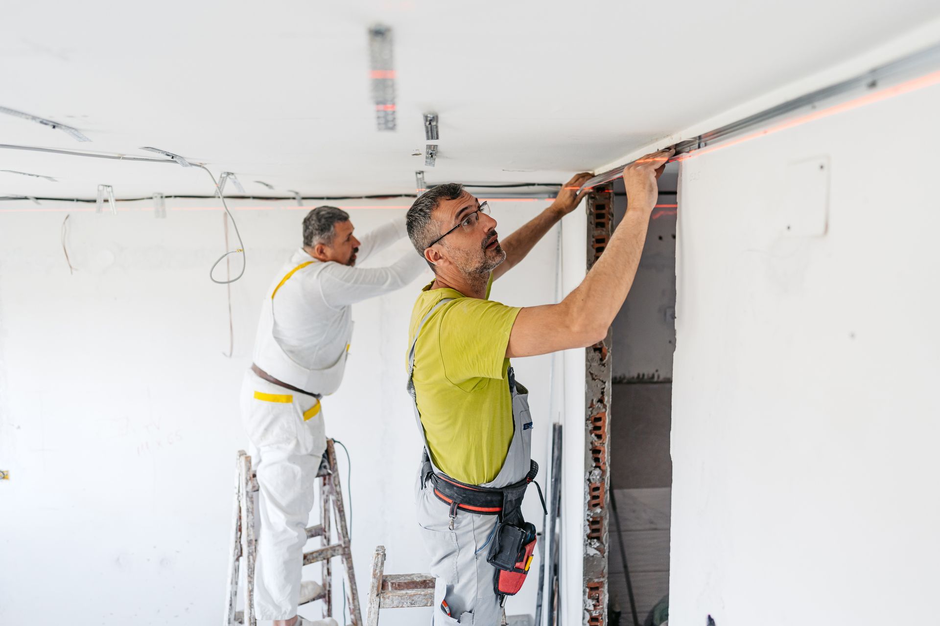 Two male remodeling contractors install a gypsum board on the ceiling of an apartment. Two male remodeling contractors install a gypsum board on the ceiling of an apartment.