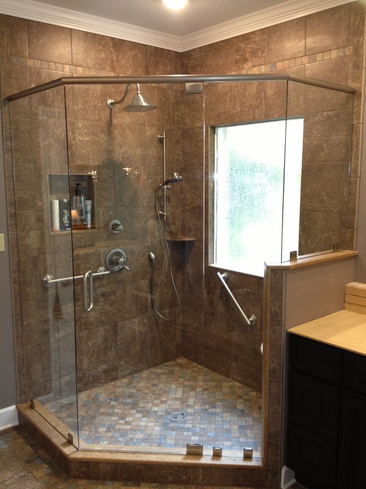 A bathroom with a walk in shower with a glass door and a window.