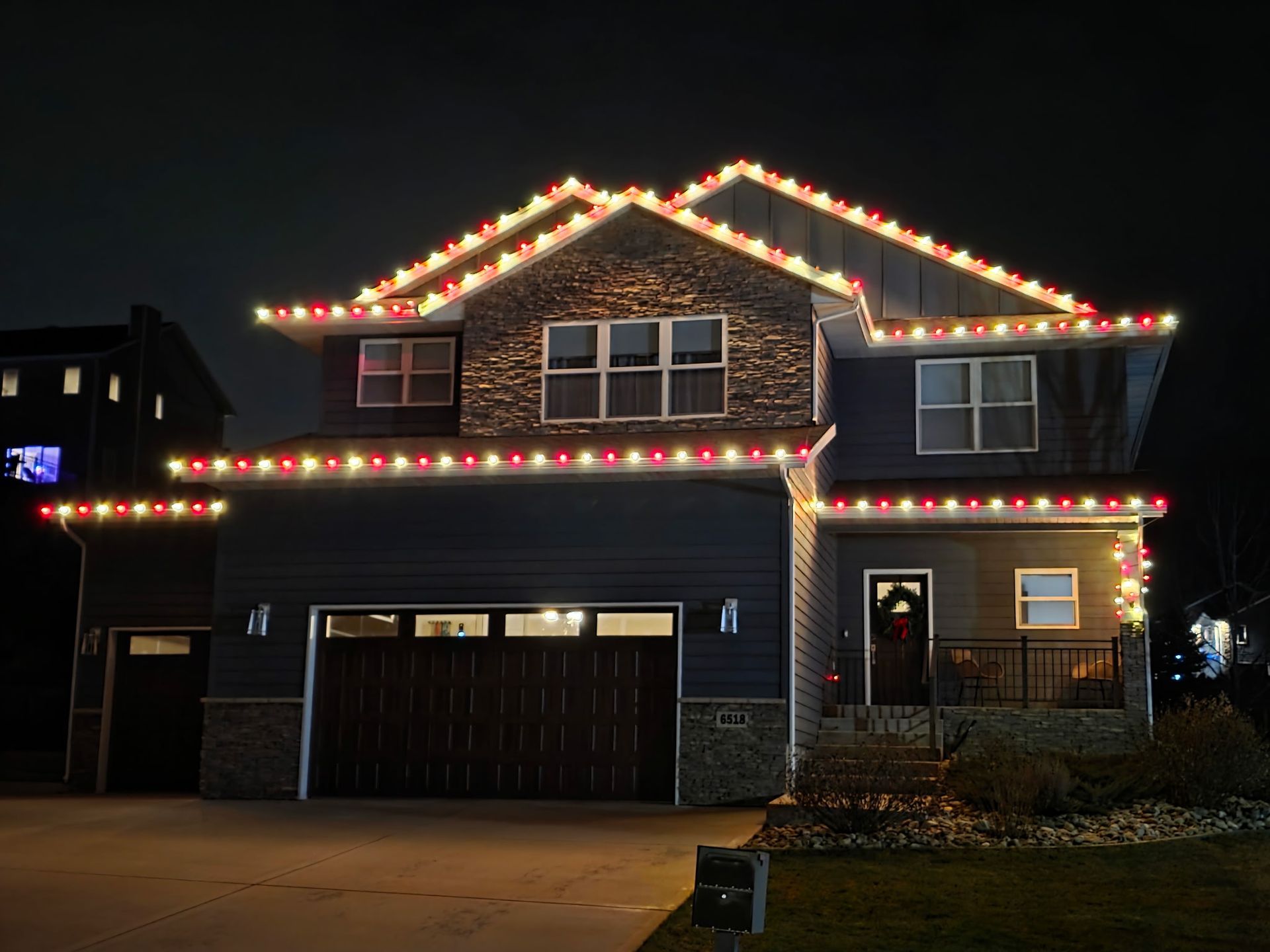 Two-story house at night, adorned with glowing red and white Christmas lights.