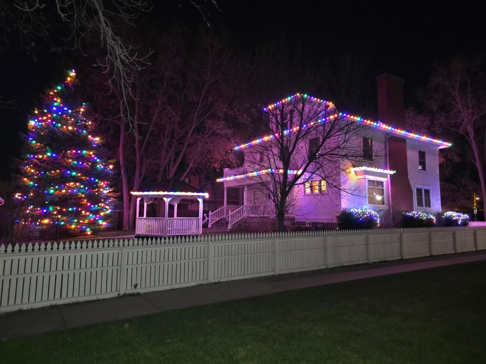 A two-story house is adorned with colorful Christmas lights, casting a festive glow.