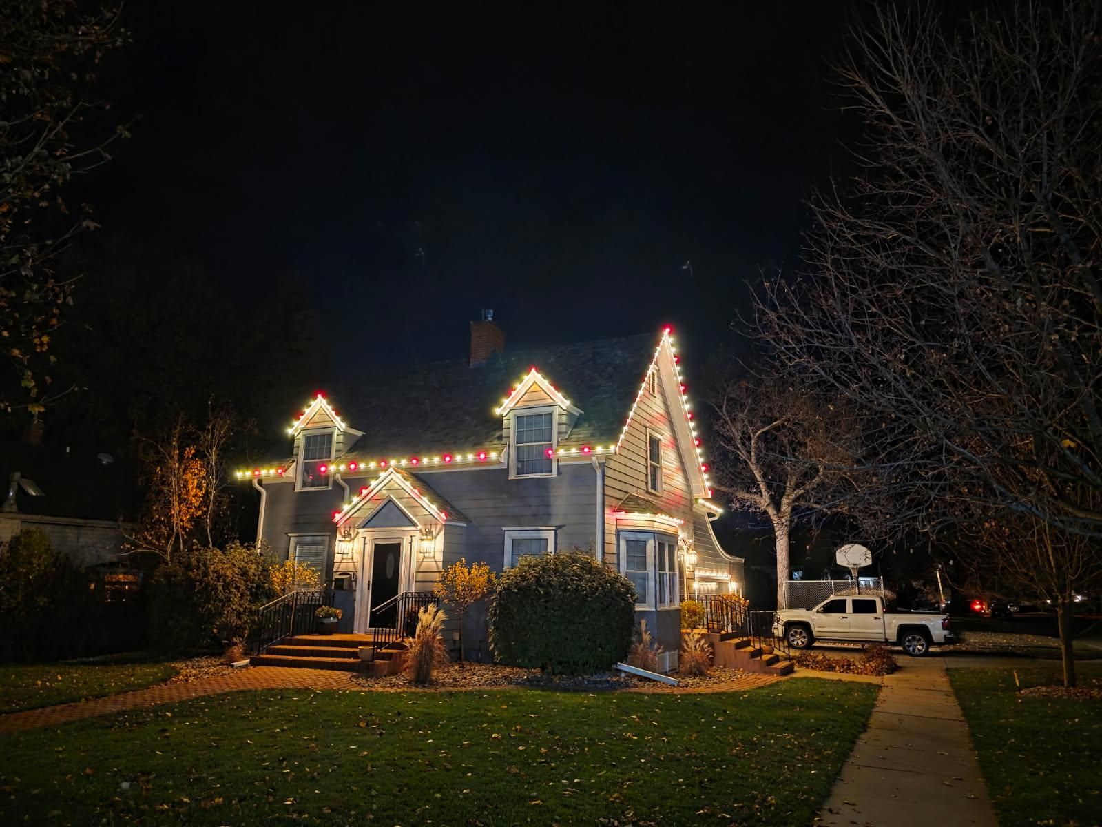 A cozy house adorned with colorful Christmas lights on the roof and windows, set against a dark night sky.
