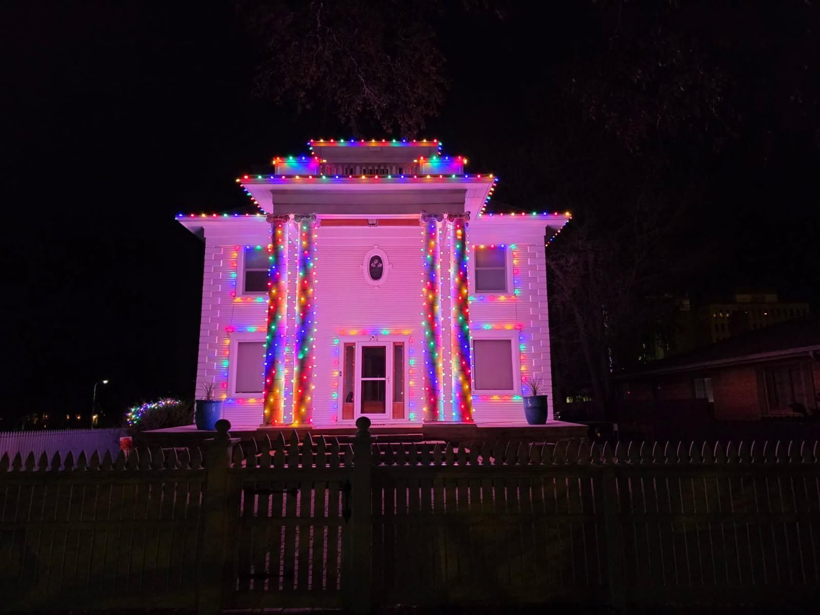 A two-story house at night adorned with colorful, vibrant holiday lights along the roof and columns.