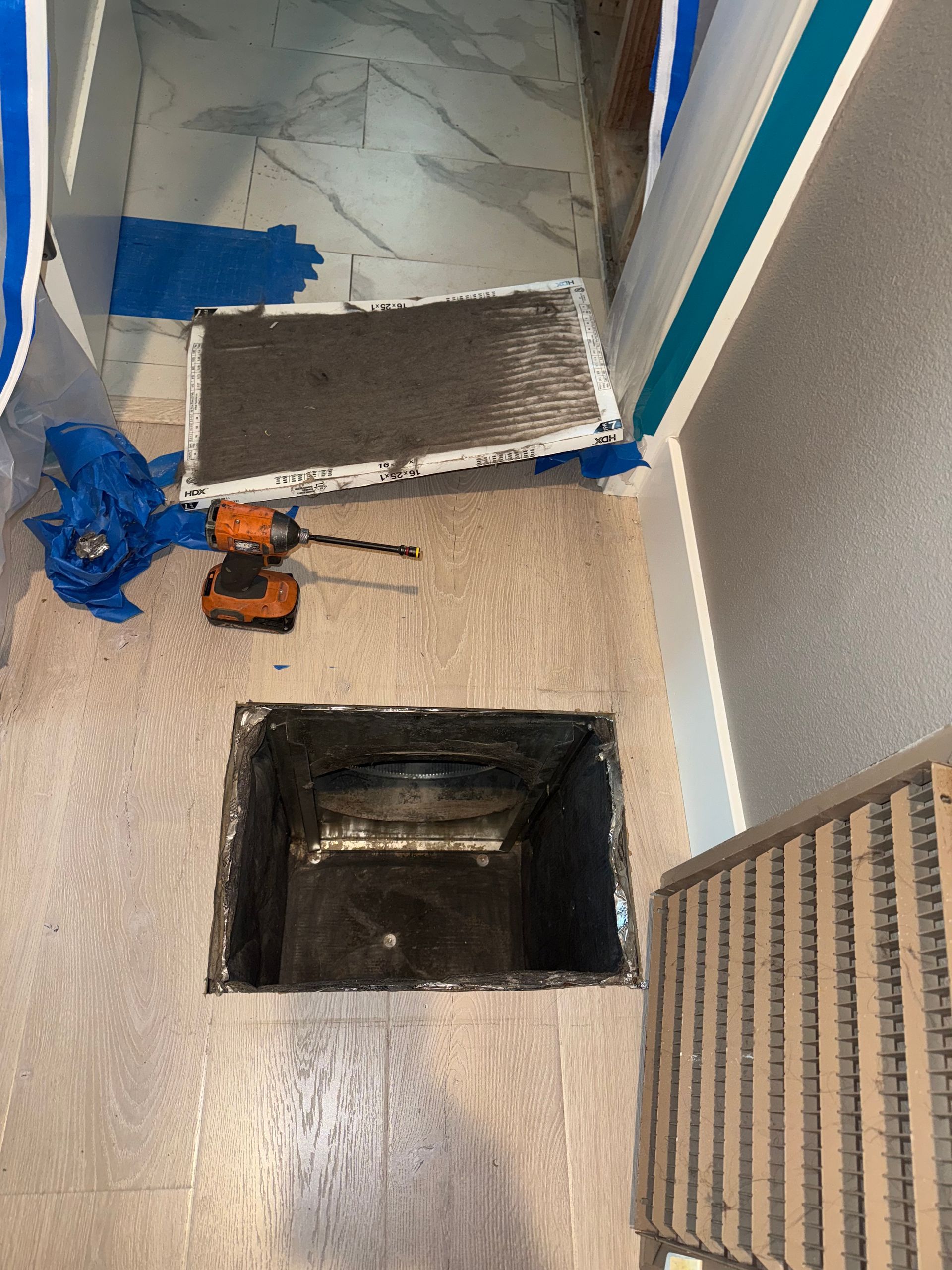 Open air vent with filter removed, surrounded by tools and debris on a light-colored floor.