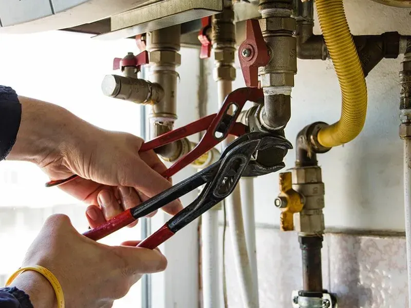 A Plumber is Fixing a Water Heater With a Pair of Pliers — Subat Plumbing Services in Kurri Kurri, NSW