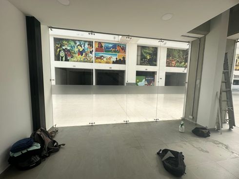Un espacio comercial vacío con paneles de arte en la pared, materiales de construcción y bolsas en el suelo.
