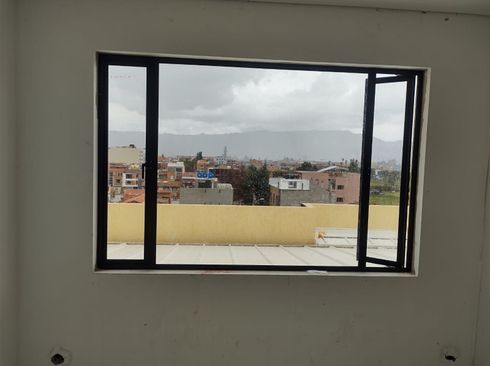 Ventana con marco negro con vista al paisaje urbano y al cielo nublado.