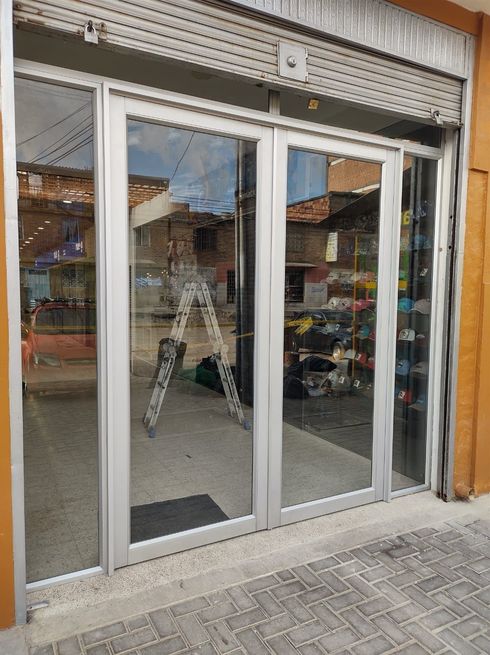 Escaparate con puertas de cristal y persianas metálicas de seguridad, en el interior de la puerta hay una escalera.