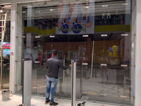 Hombre abriendo la puerta de cristal de una tienda. Interior del edificio, letrero visible. Obras en curso.
