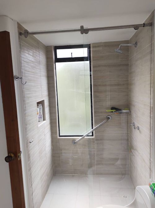 Baño con ducha de cristal, barras de apoyo, ventana y azulejos.