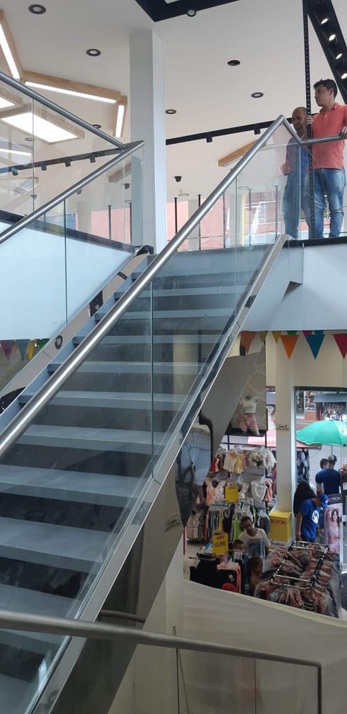 Escalera con barandilla de cristal en una tienda. Gente de pie en la planta superior, con banderines coloridos y artículos de la tienda a la vista.