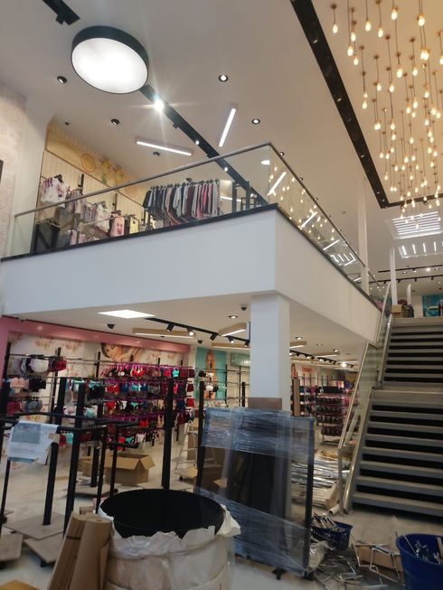 Interior de una tienda minorista con un segundo piso; materiales de construcción visibles en primer plano.