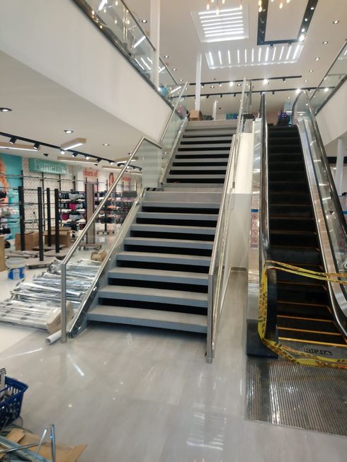 Interior de una tienda con escalera y escalera mecánica. Escaleras grises con barandilla de cristal.