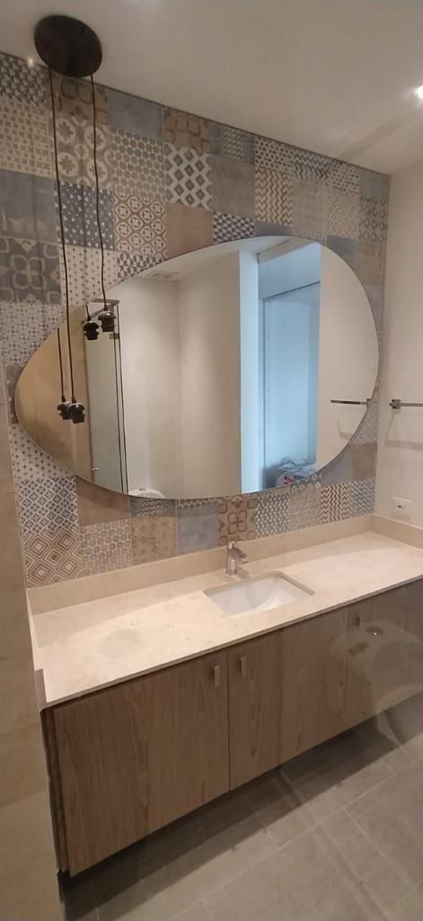 Baño con tocador de madera, espejo ovalado y salpicadero de mosaico.