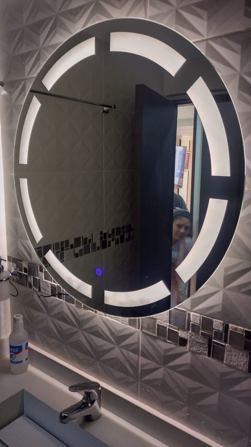Espejo de baño circular iluminado por LED; se refleja una persona.