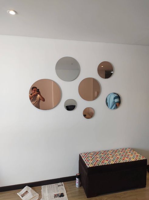 Pared blanca con un grupo de espejos redondos, banco marrón debajo; persona reflejada en los espejos.