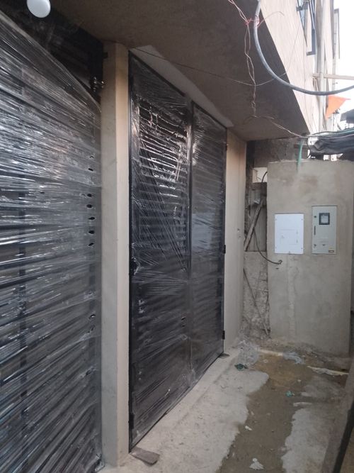 Exterior de un edificio con dos puertas negras plastificadas y un callejón lateral. Cuadro eléctrico a la derecha.
