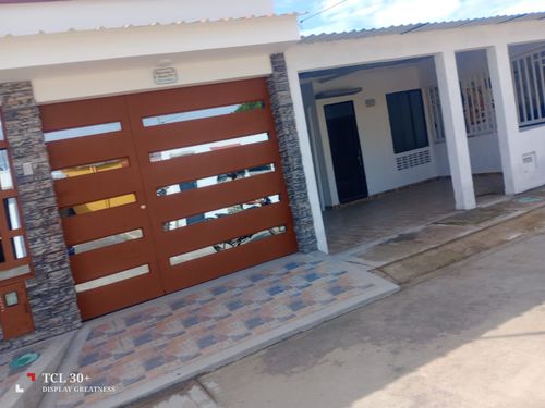 Una casa cerrada de color marrón con molduras y ventanas blancas, una entrada gris y un día soleado.