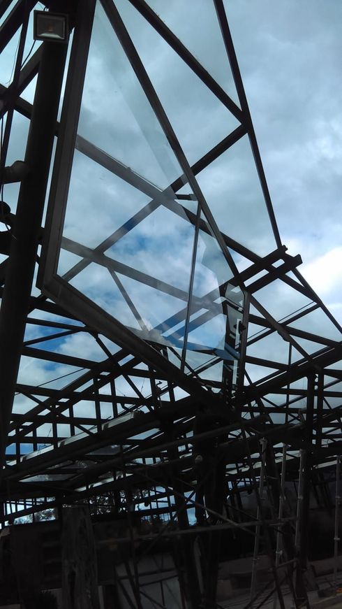 Un panel de vidrio que se instala en una estructura de techo con marco de metal oscuro contra un cielo nublado.
