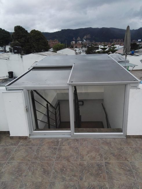 Acceso a la escalera de la azotea con puertas de vidrio y techo oscuro, con vista al paisaje urbano y las montañas.