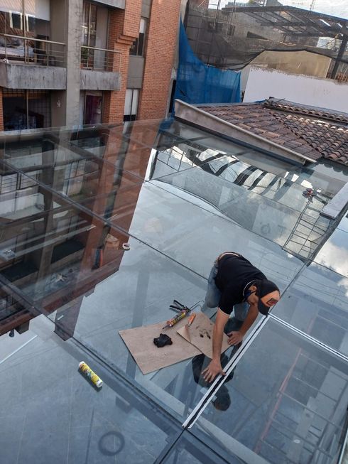 Hombre trabajando en un tejado de cristal, con herramientas sobre cartón. Exterior del edificio al fondo.