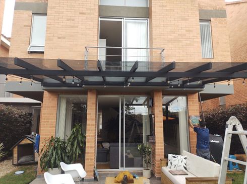 Exterior de casa de ladrillo con marquesina, patio y puerta corrediza de vidrio abierta.