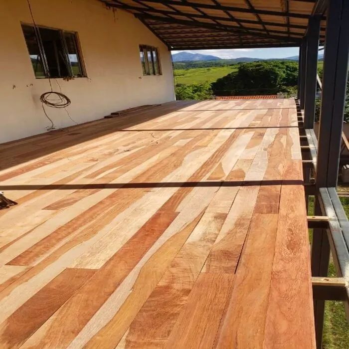 Deck de madeira sob uma varanda coberta com vista para uma paisagem verdejante.