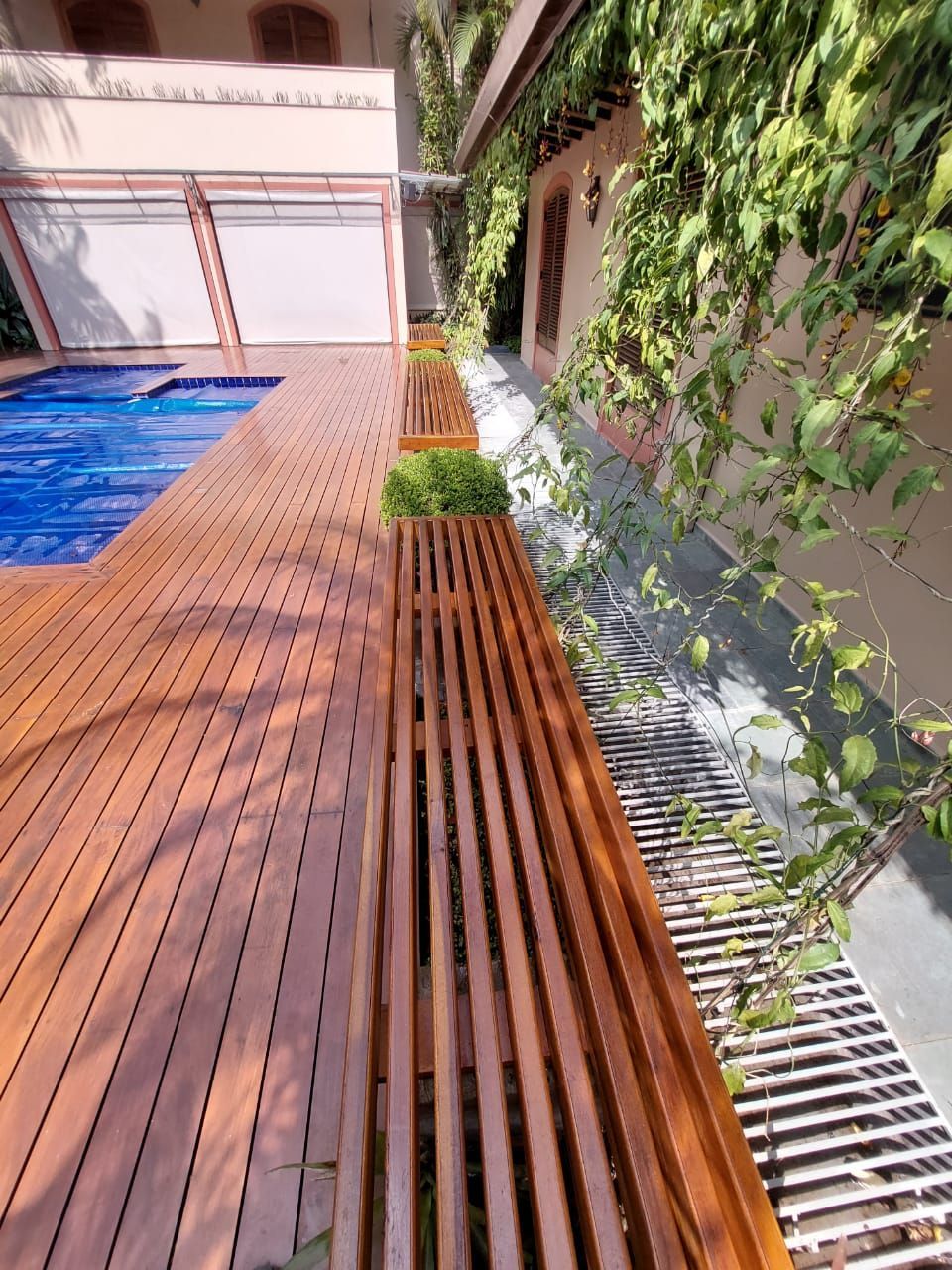 Deck de madeira da piscina com um banco ao lado de uma parede coberta de trepadeiras verdes.