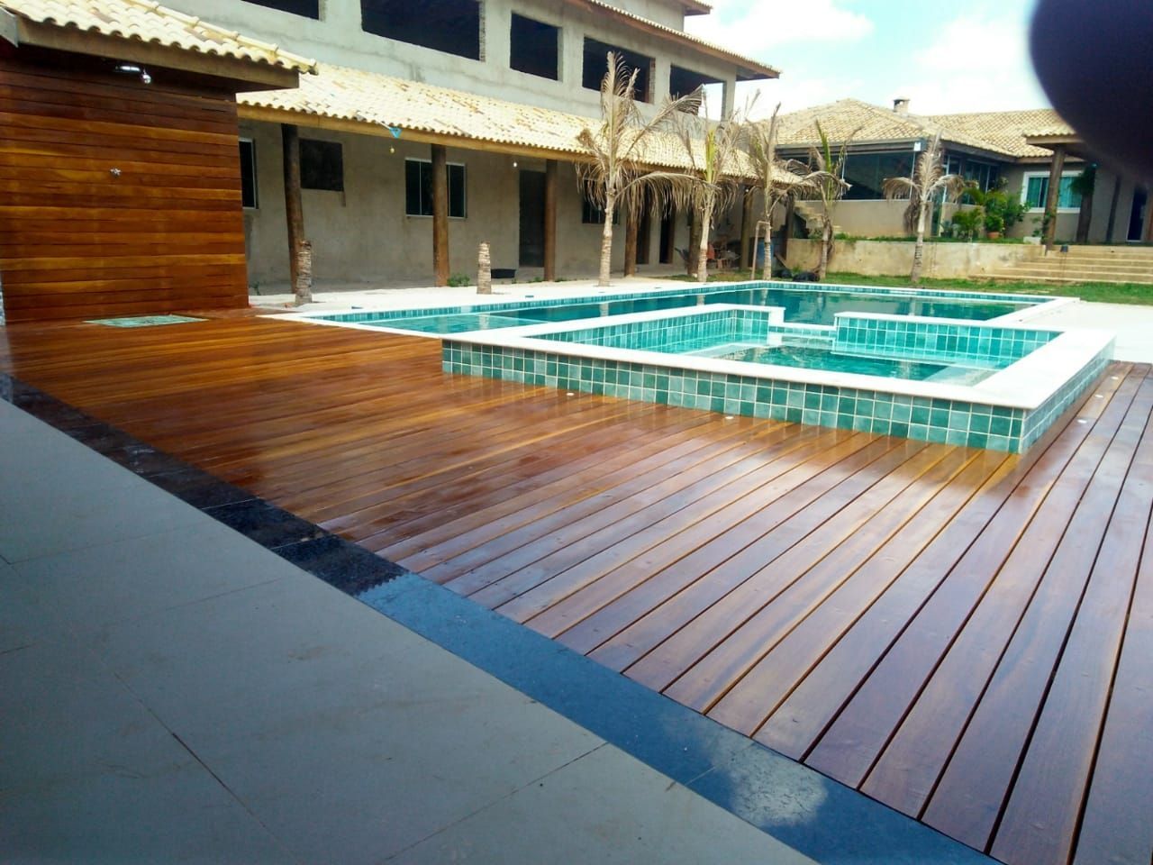 Deck de madeira circundando uma piscina revestida de azulejos em uma casa grande.