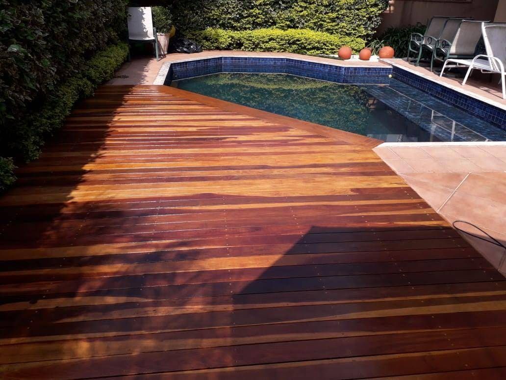 Deck de madeira ao lado de uma piscina de água azul, rodeado de vegetação e com assentos.