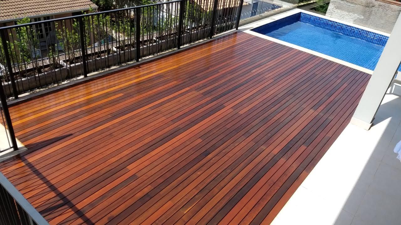 Deck de madeira com uma pequena piscina, corrimão preto e vegetação exuberante.
