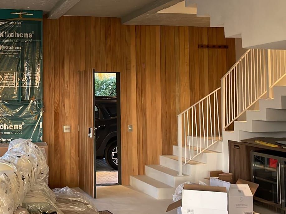Interior com painéis de madeira, escadas com corrimão branco, uma porta que revela um carro e materiais de construção.