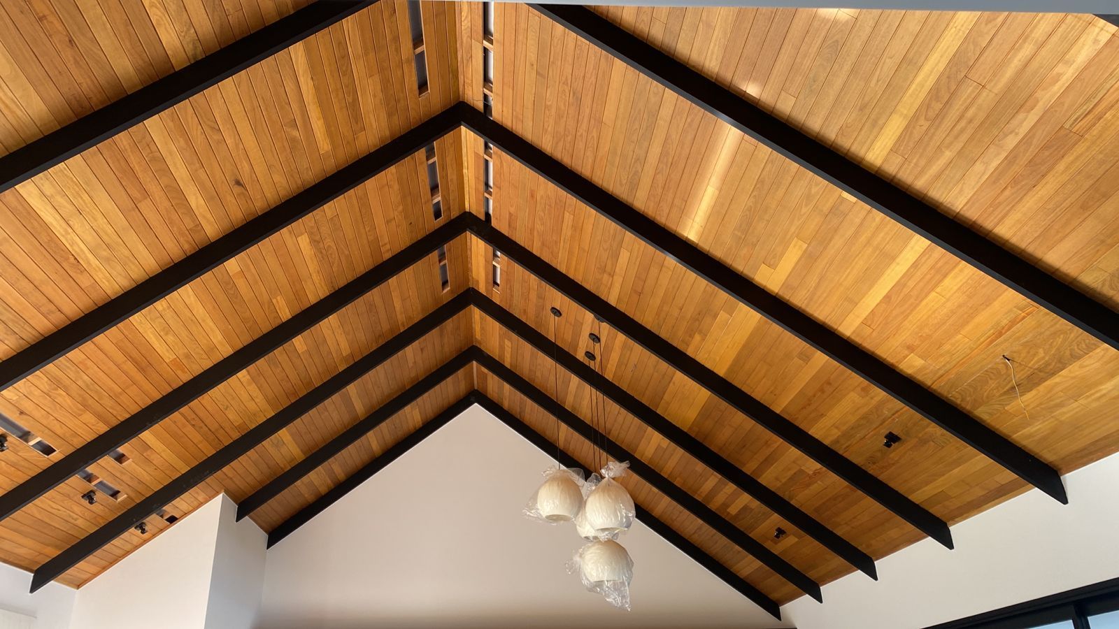 Teto abobadado de madeira com vigas pretas. Luminária suspensa abaixo.