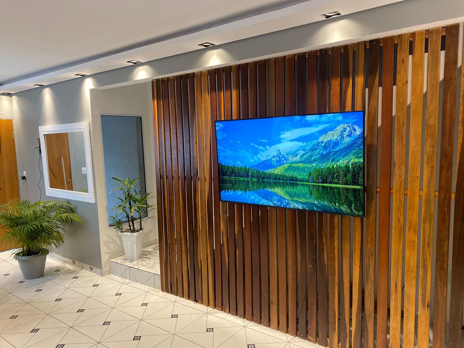 Sala de estar com parede de ripas de madeira, TV, espelho e plantas.