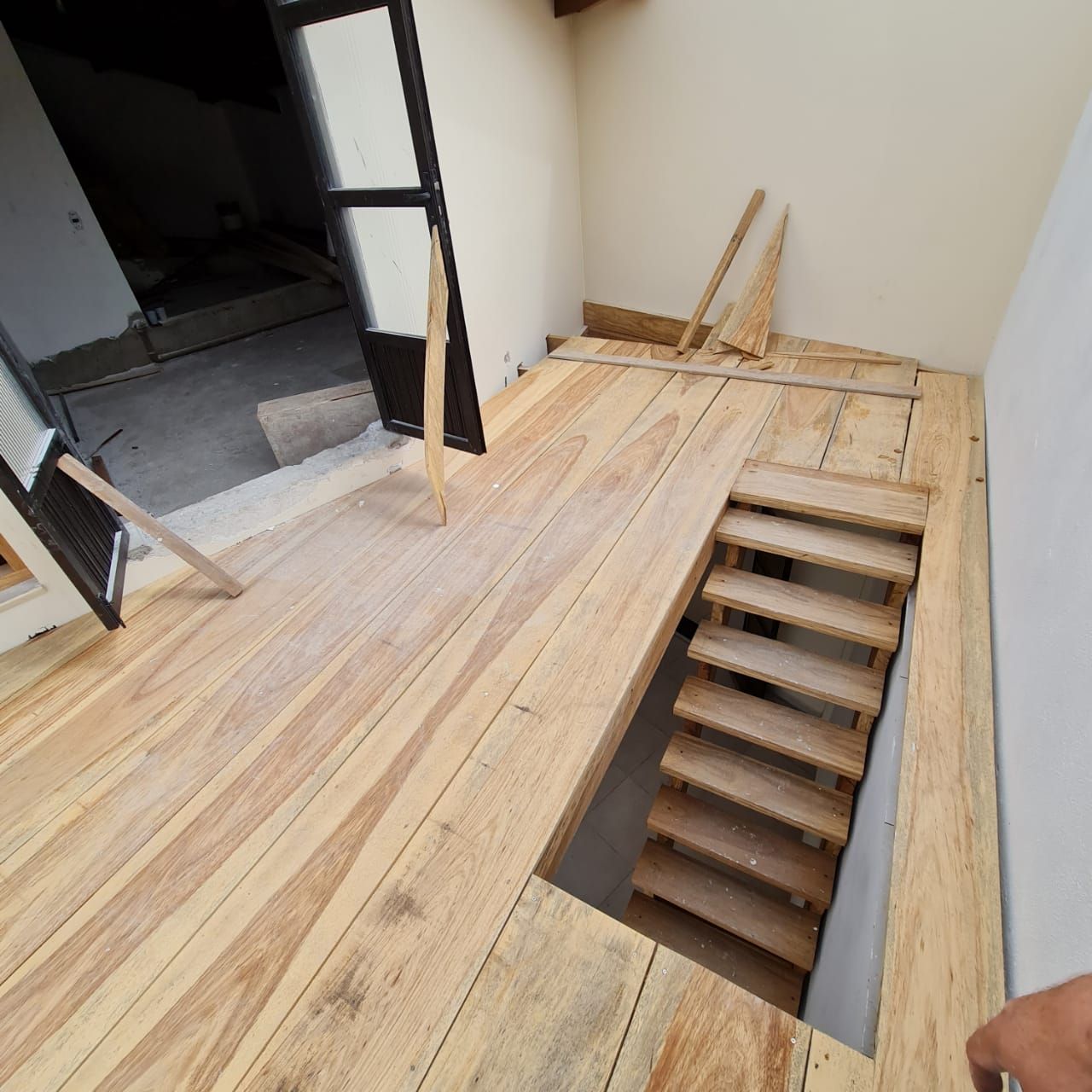 Piso de madeira com escada que desce para um recanto, porta visível ao fundo.