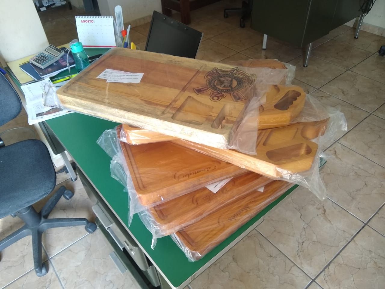 Pilha de bandejas de madeira, algumas envoltas em plástico, sobre uma mesa verde.