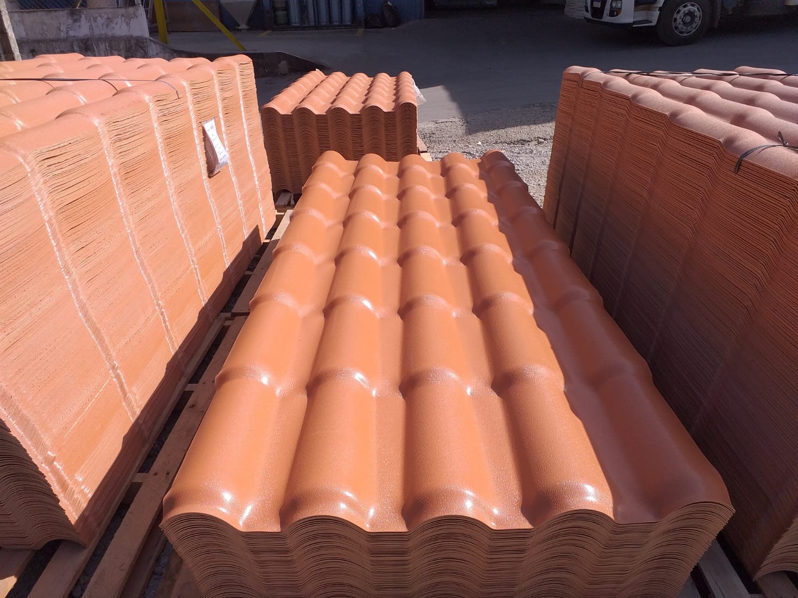 Pilhas de telhas de cor terracota, prontas para instalação, sobre paletes de madeira ao ar livre.