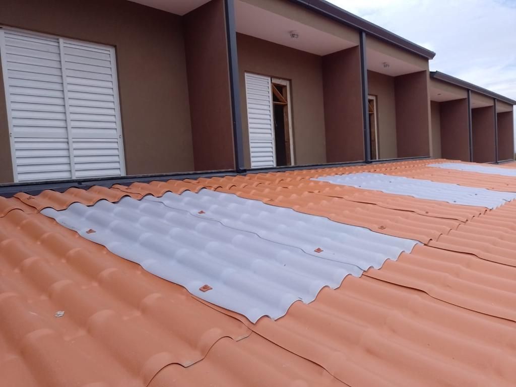 Telhado de telhas de terracota com seções onduladas cinzentas. Prédio com paredes e varandas marrons.