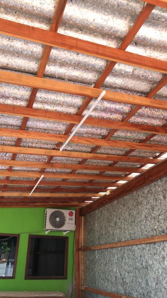 Telhado com estrutura de madeira e painéis ondulados cinza. Interior com paredes verdes, ar condicionado e janelas.