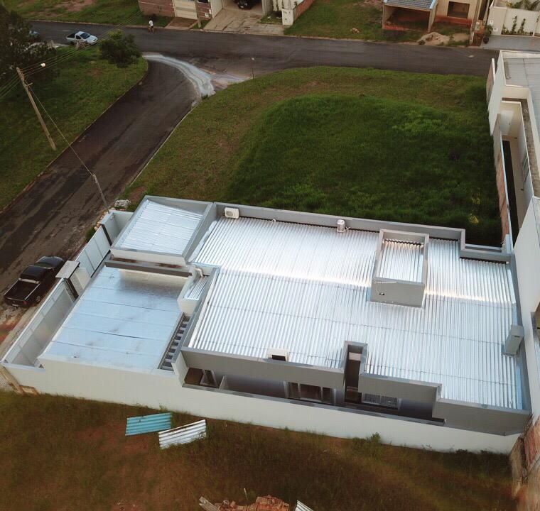 Vista aérea de uma casa moderna com telhado de metal ondulado. A casa fica em uma colina gramada.