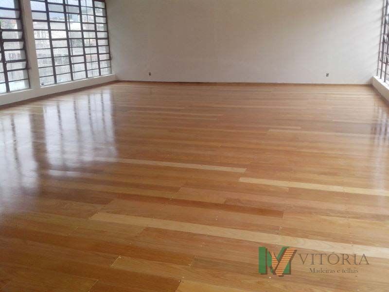 Quarto vazio com piso de madeira polida e grandes janelas.