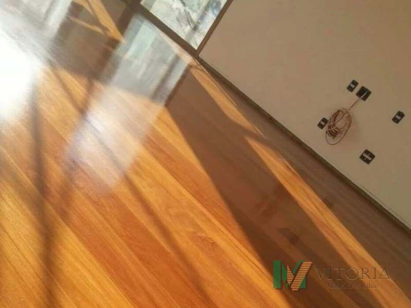 Piso de madeira com reflexo de luz, ao lado de uma parede branca com ventilador de teto.