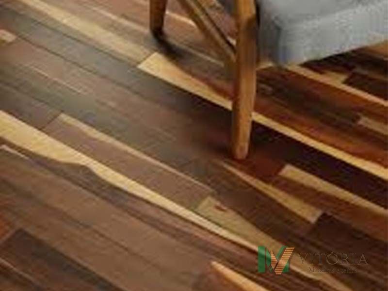 Piso de madeira com tábuas de cores variadas e um pé de cadeira.