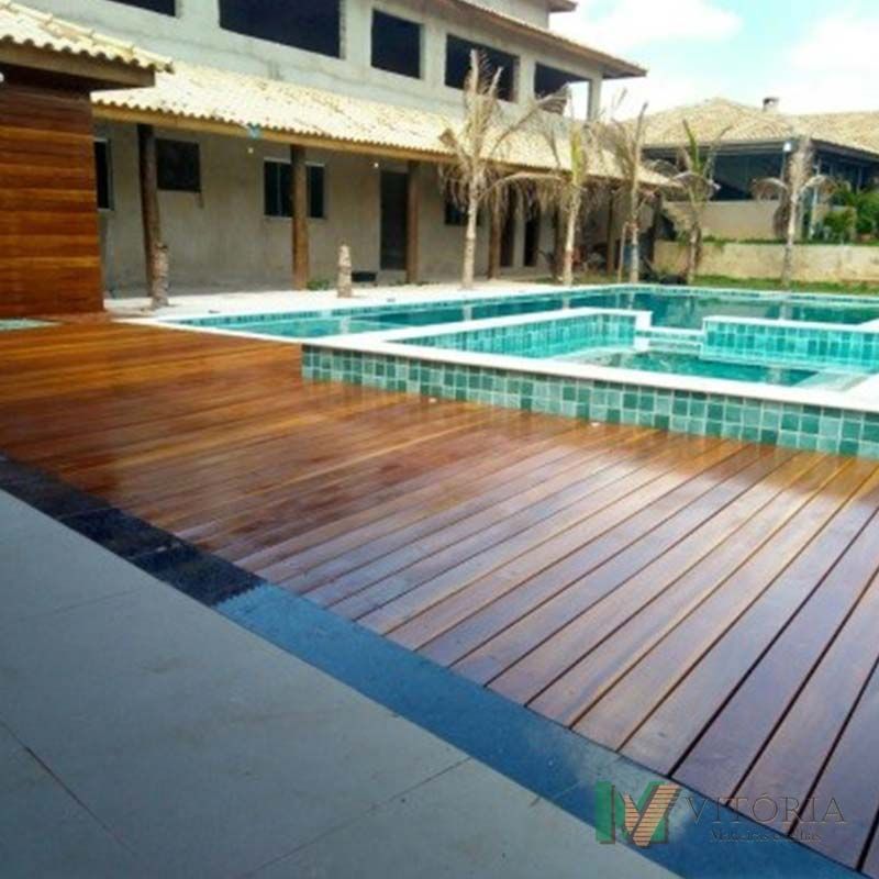 Deck de madeira ao lado de uma piscina com água turquesa. Uma grande casa ao fundo.