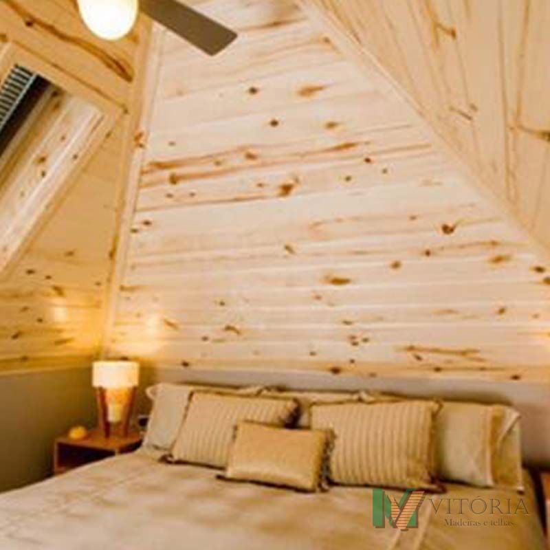 Quarto com paredes e teto revestidos de madeira, uma cama com travesseiros e um abajur.