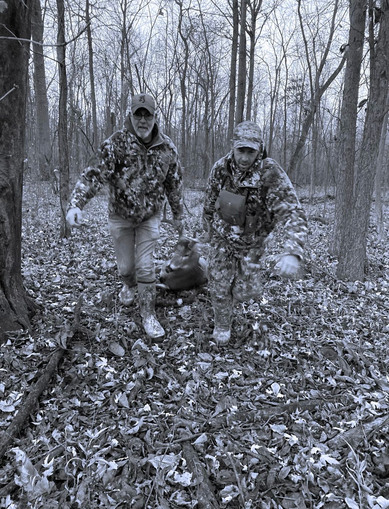 A black and white photo of two men walking through a forest.