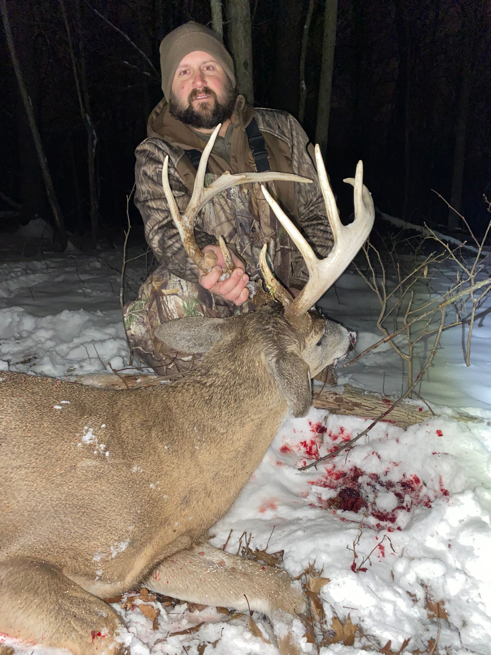 A man is kneeling down next to a large deer in the snow.
