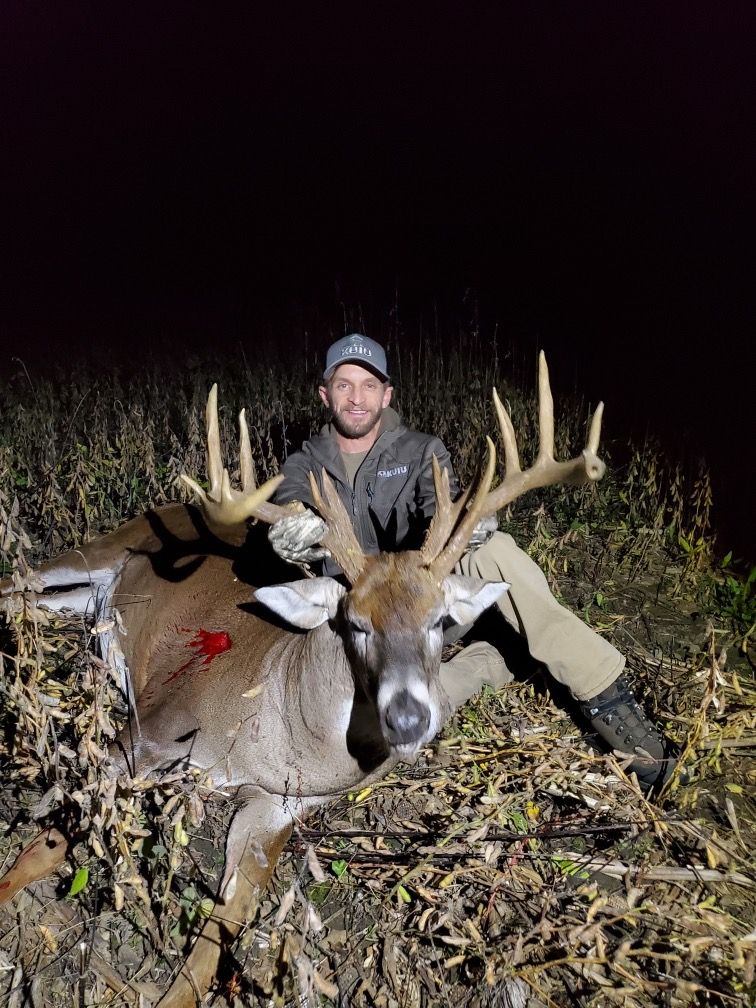 A man is sitting next to a large deer in a field.
