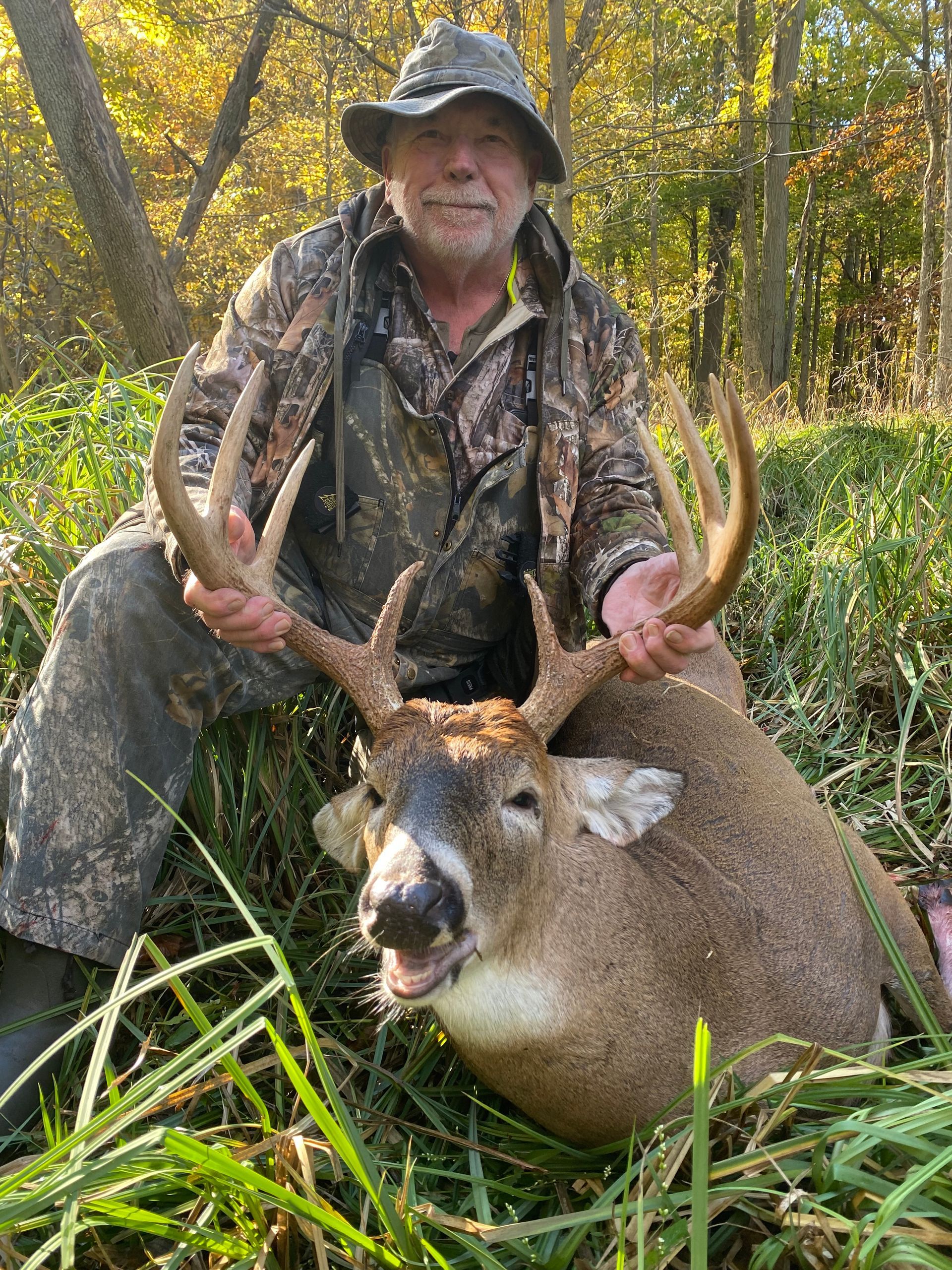 A man is kneeling down next to a deer in the woods.